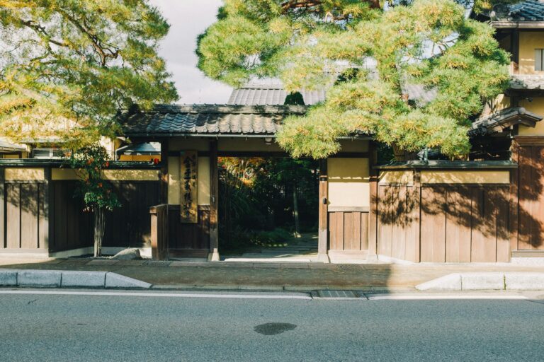 A serene Japanese entrance framed by lush trees, showcasing traditional wooden architecture and cultural elements.